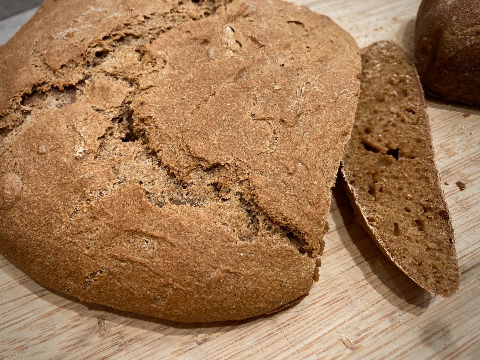 A round loaf of whole wheat bread on a wooden cutting board.