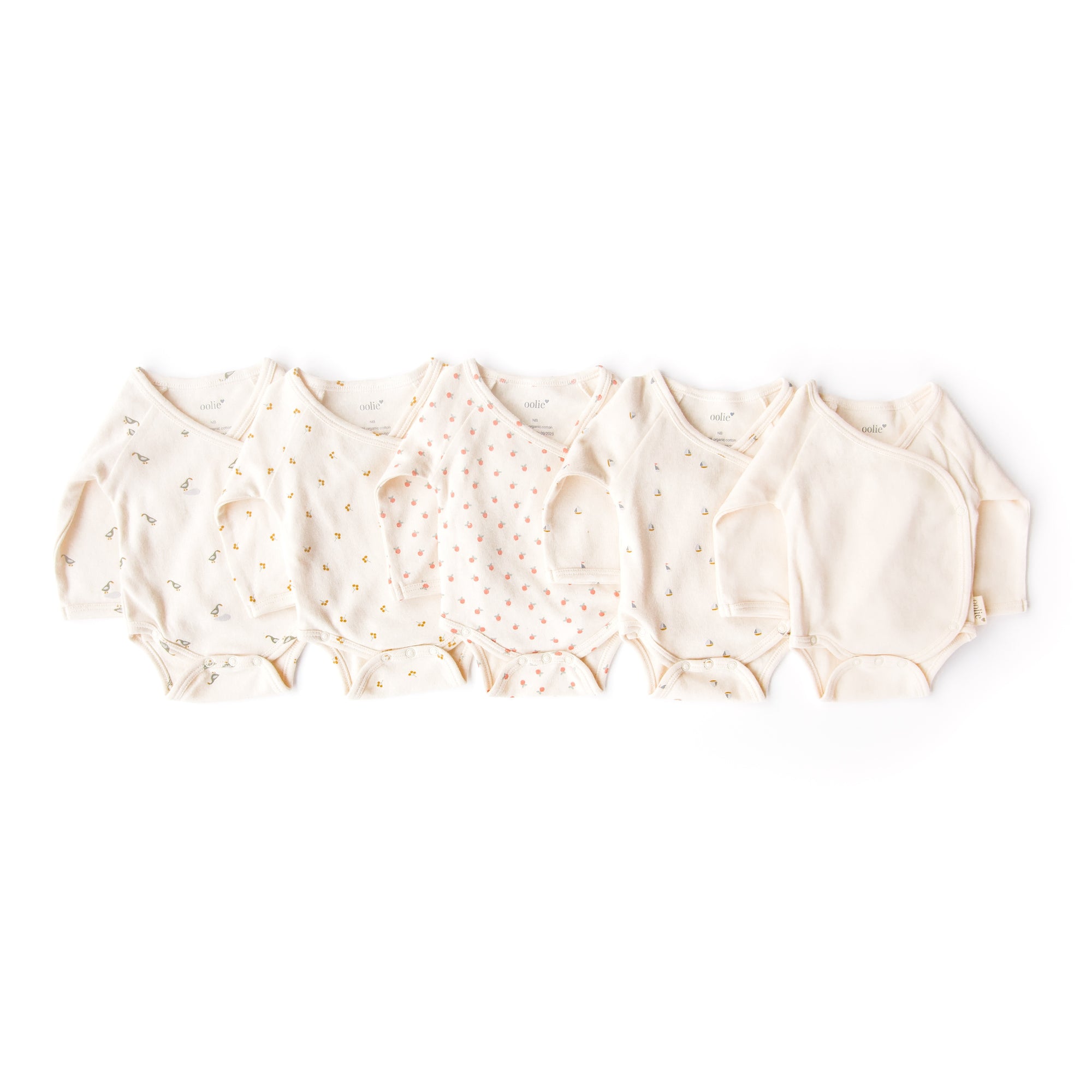 Oolie organic baby onesies in five different graphic prints, gently folded on a white background.