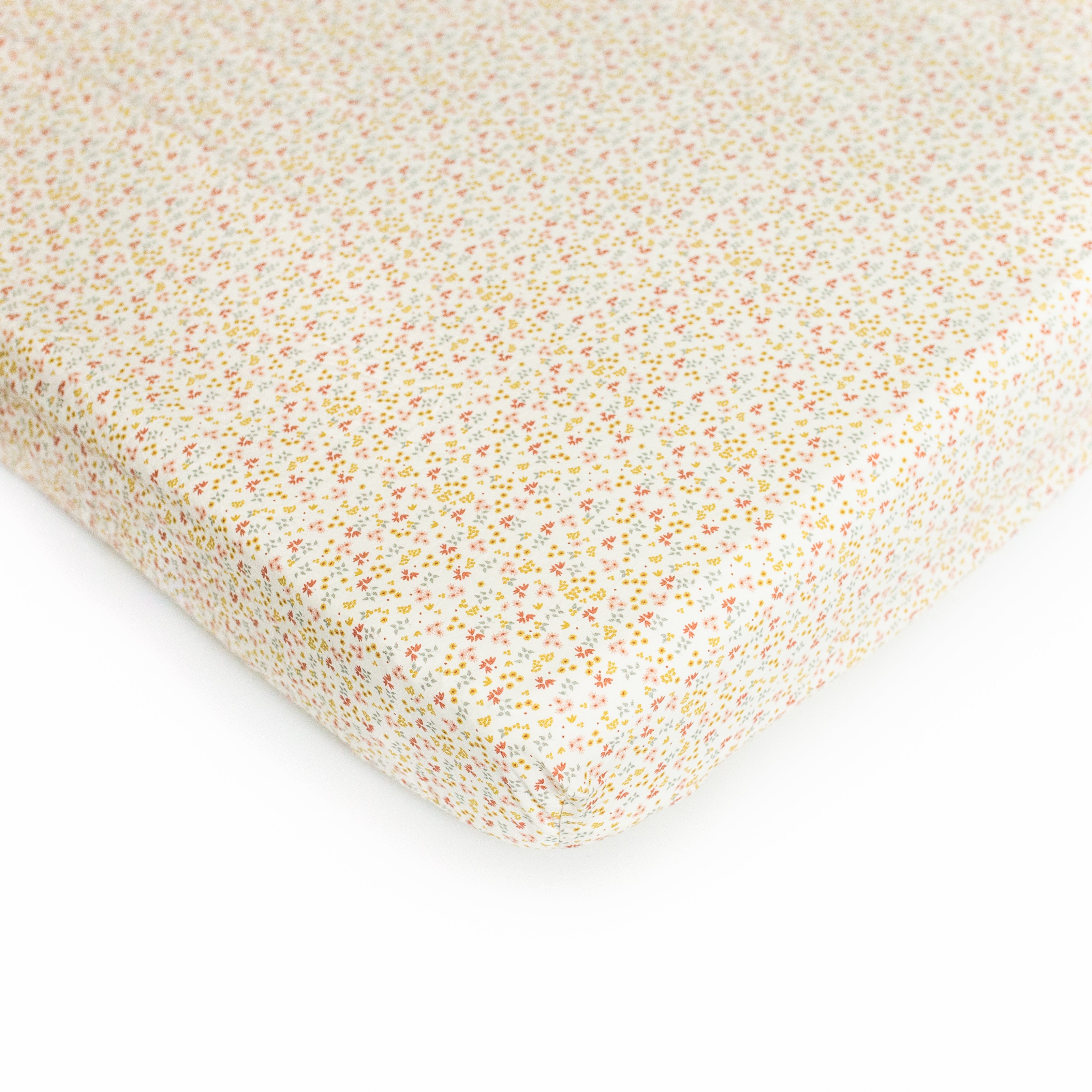 An Oolie organic cotton crib sheet with the prairie print, a natural color with very small flowers.
