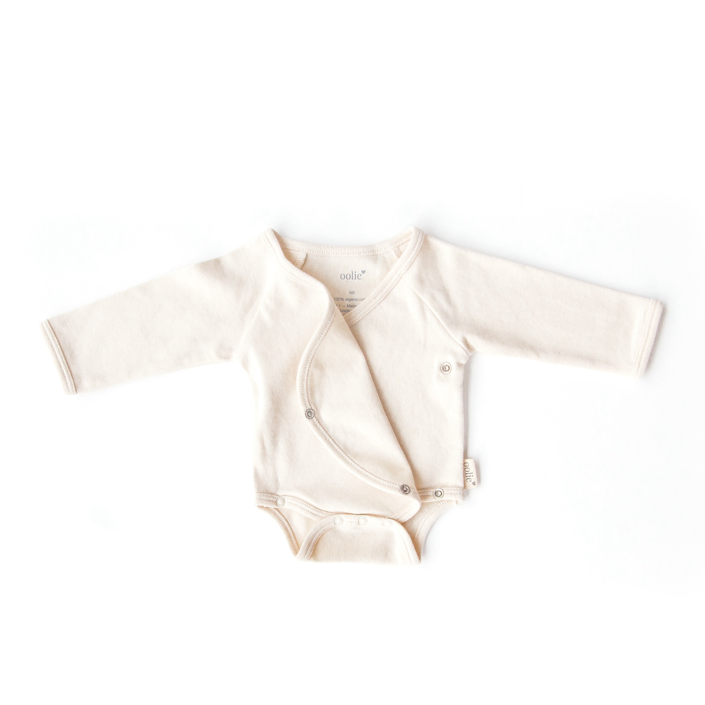 A natural color, Oolie organic cotton onesie, laid flat on a white background, with initial snaps unsnapped and the onesie's front flap folded back, kimono-style.