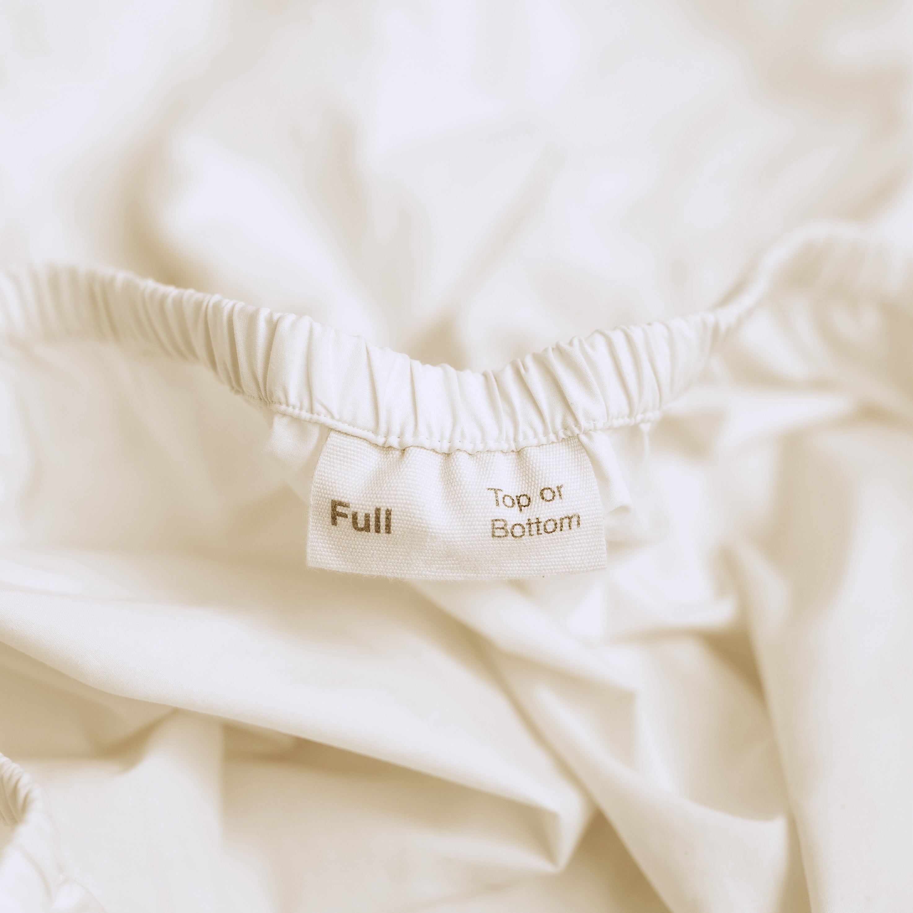 A detail view of the orientation label on an Oolie fitted sheet, indicating &quot;Full&quot; size and marking the &quot;Top or Bottom&quot; of the sheet.