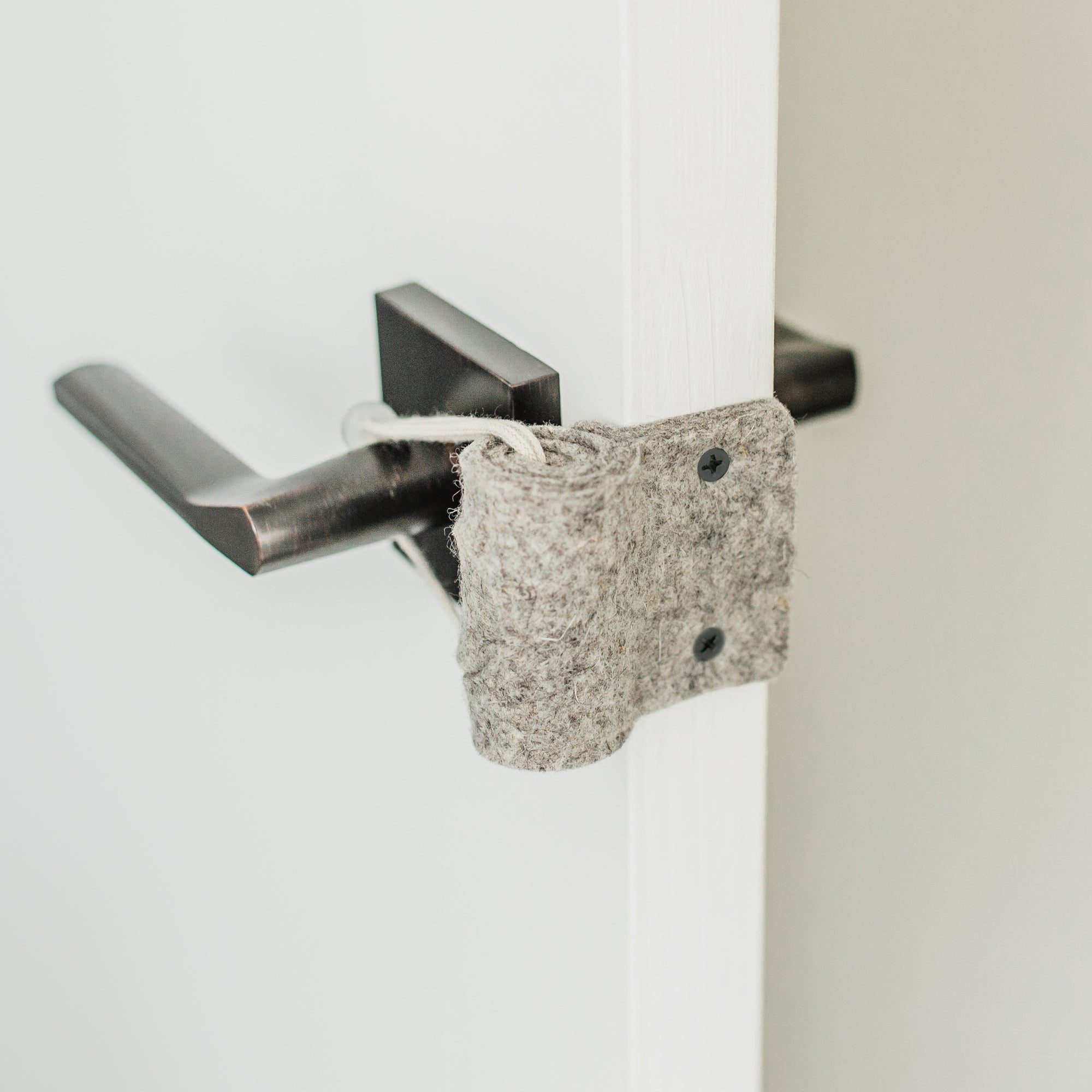 The Oolie Shoosh door silencer and safety bumper shown installed on a door. Two screws keep the Shoosh firmly in place, attached to the door plate, and a cord is snugly looped around the door handle.