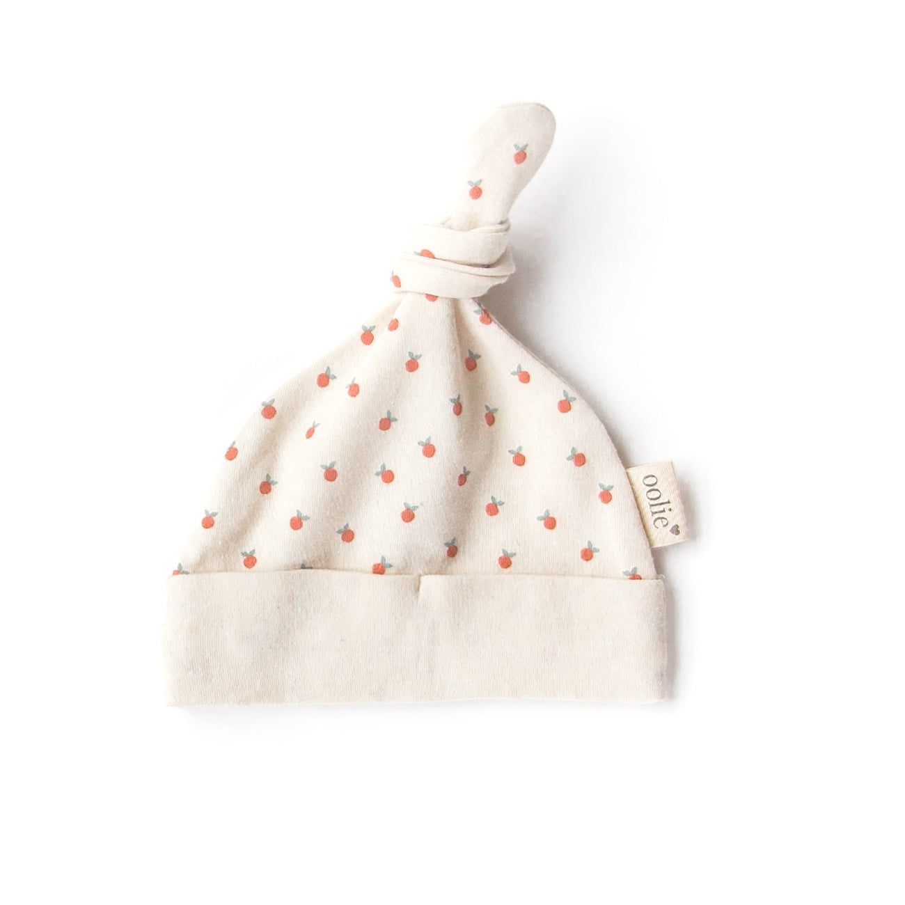 An Oolie organic cotton top knot baby hat with the little peach print, a natural color with tiny, irregular peaches in a repeating pattern.