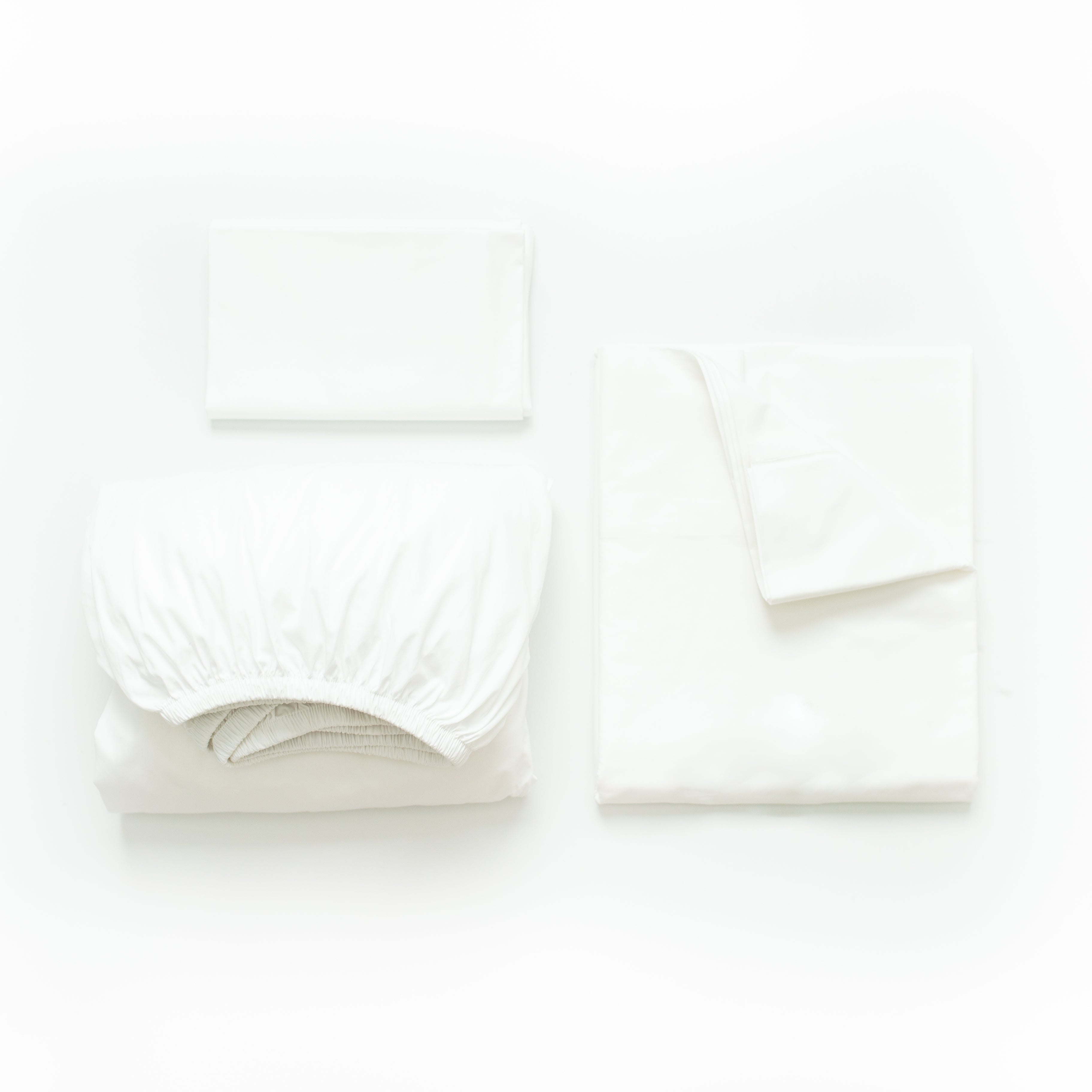 Oolie organic cotton pillowcases, flat sheet, and deep fitted sheet in white cotton, folded flat on a white background.
