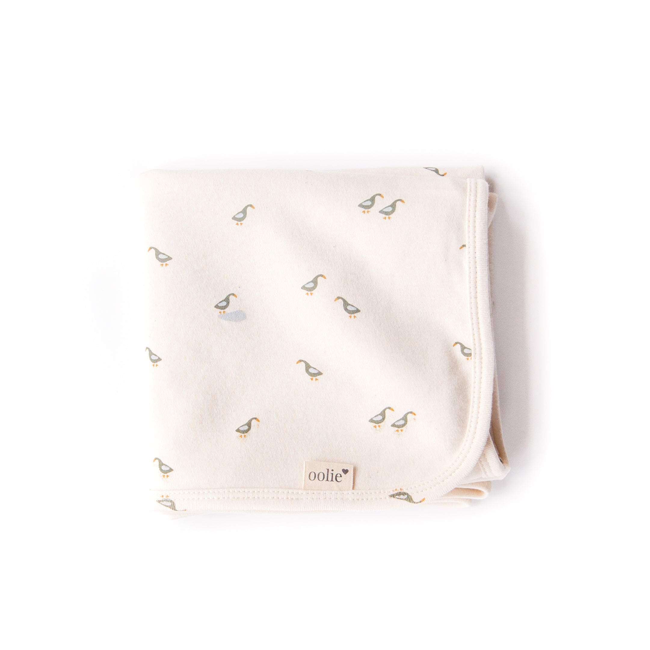 An Oolie organic cotton baby blanket with the runner ducks print, a natural color with small green and blue ducks in a repeating pattern.