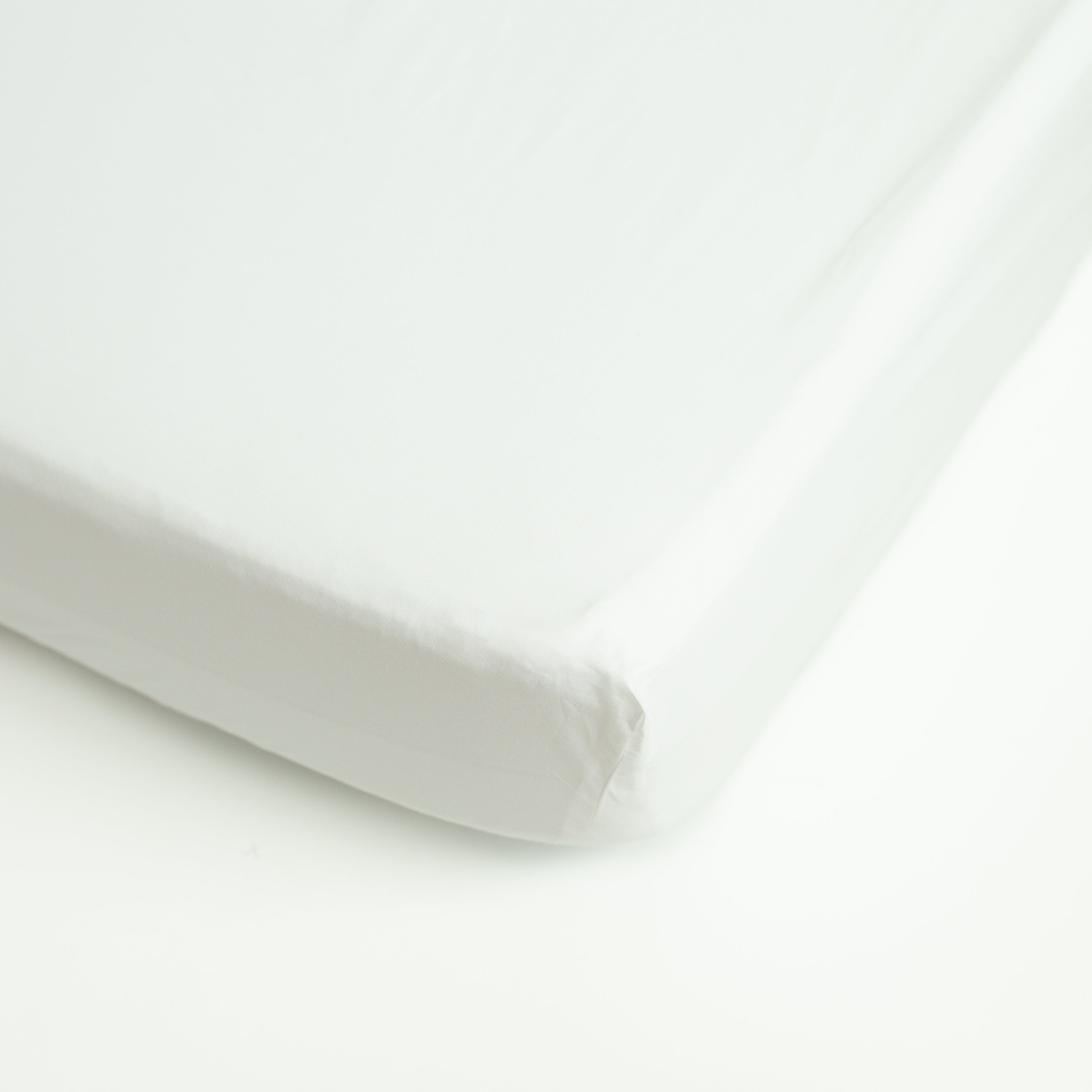 A detail view showing the soft texture of an Oolie deep fitted sheet in white cotton installed on a bed.