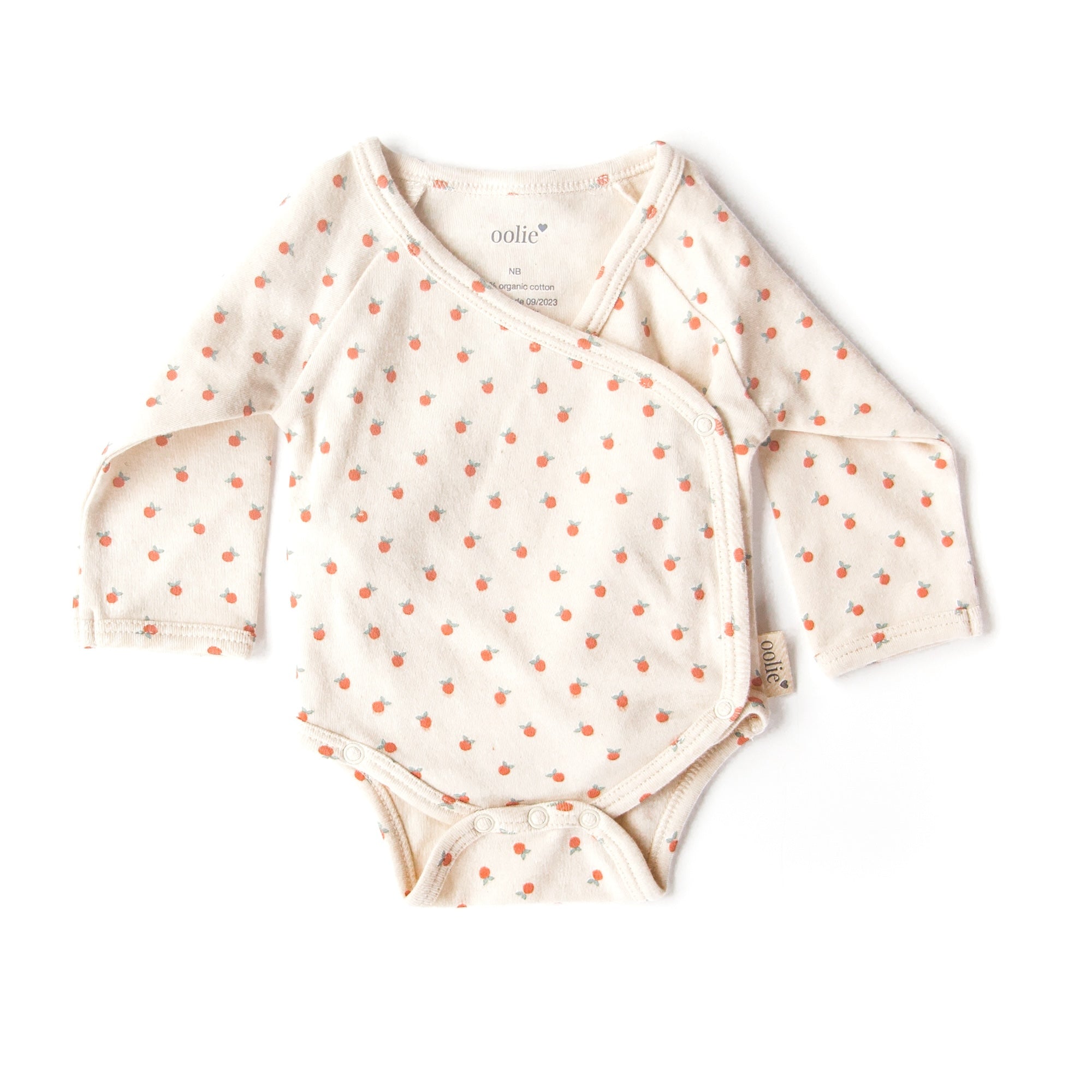 An Oolie organic cotton onesie with the little peach print, a natural color with tiny, irregular peaches in a repeating pattern.