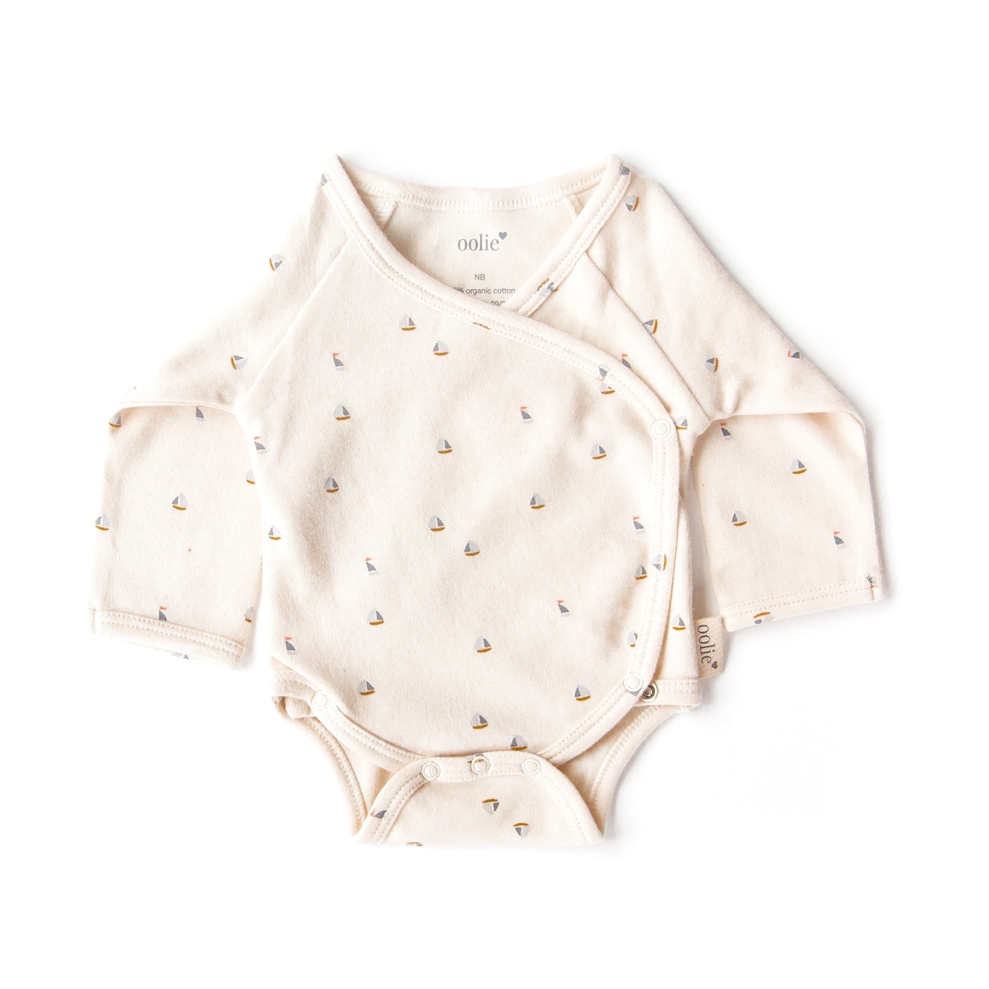 An Oolie organic cotton onesie with the schooner print, a natural color with small sailboats in a repeating pattern.