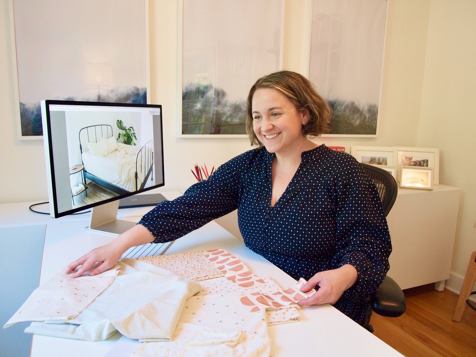 A woman smiling and looking ahead at fabric samples on a clean, modern workspace.
