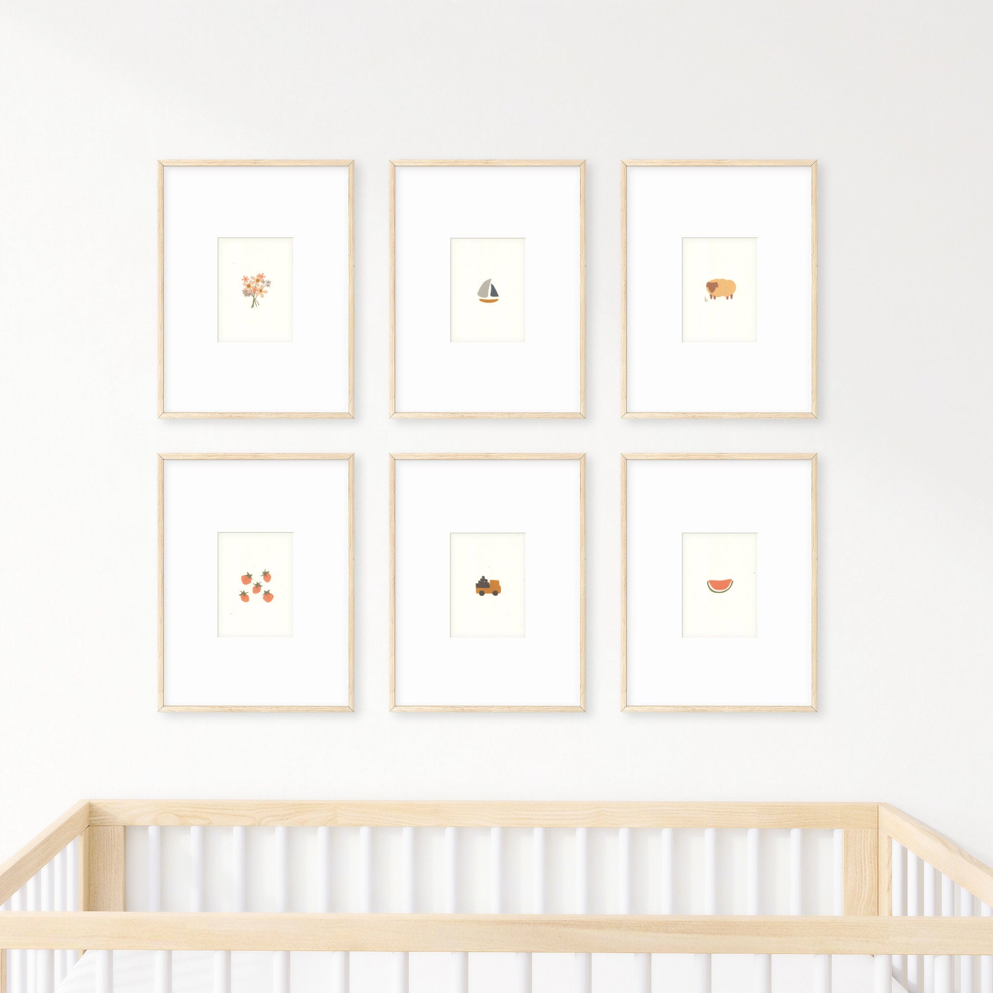 Six cute nursery prints framed and hanging on a wall over a baby's crib. The prints show: a bouquet of flowers, a small sailboat, a brown sheep, five strawberries, a small dump truck carrying boulders, and a slice of watermelon.
