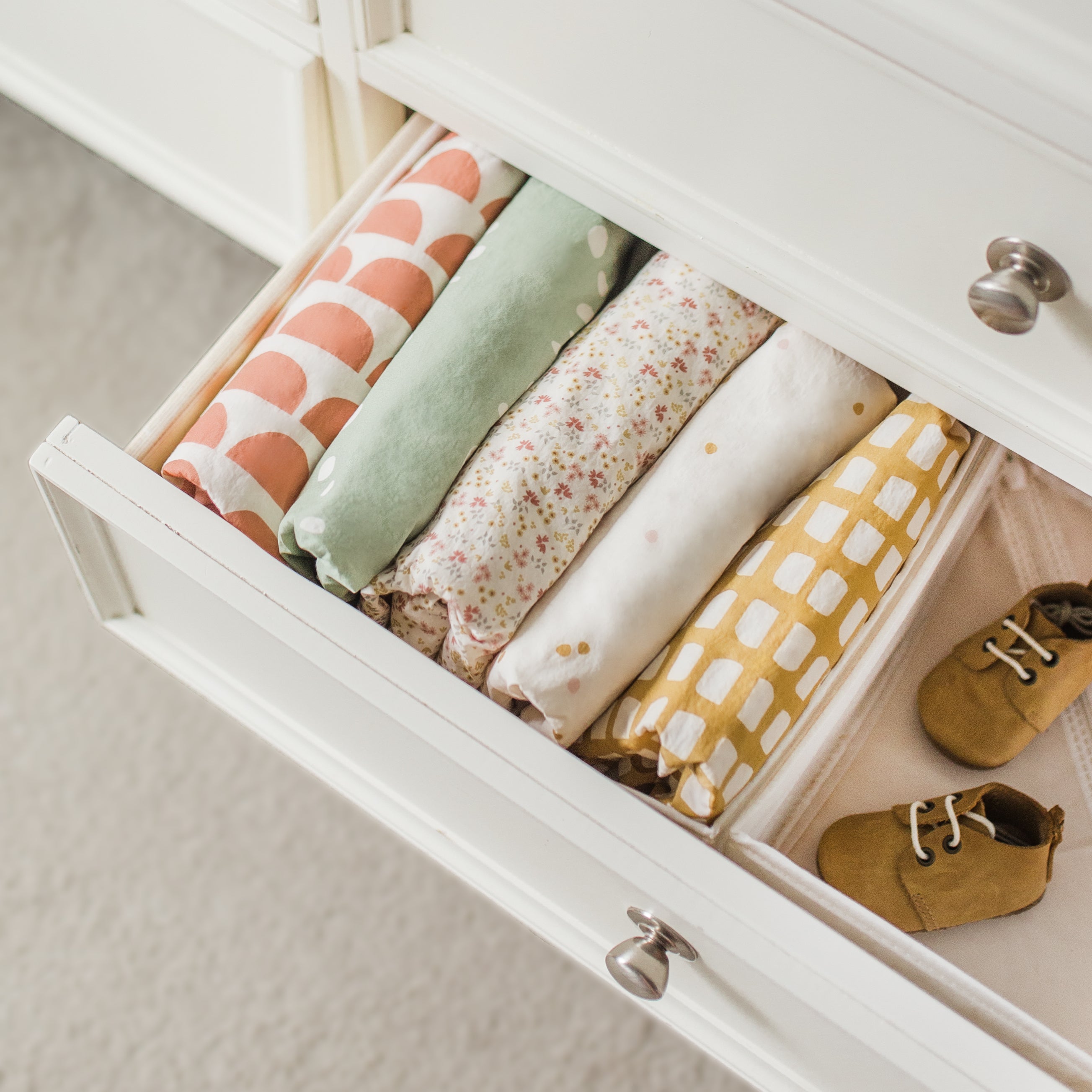 Oolie organic cotton crib sheets in five different graphic prints, gently folded and tucked into a dresser drawer.