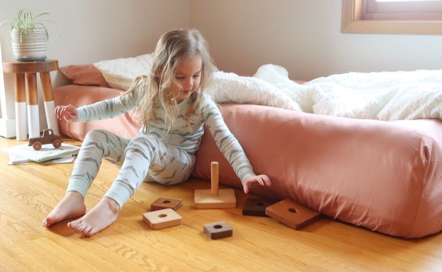 Preschooler playing with blocks on the floor, leaning against a floor bed with Oolie Base and Bolster