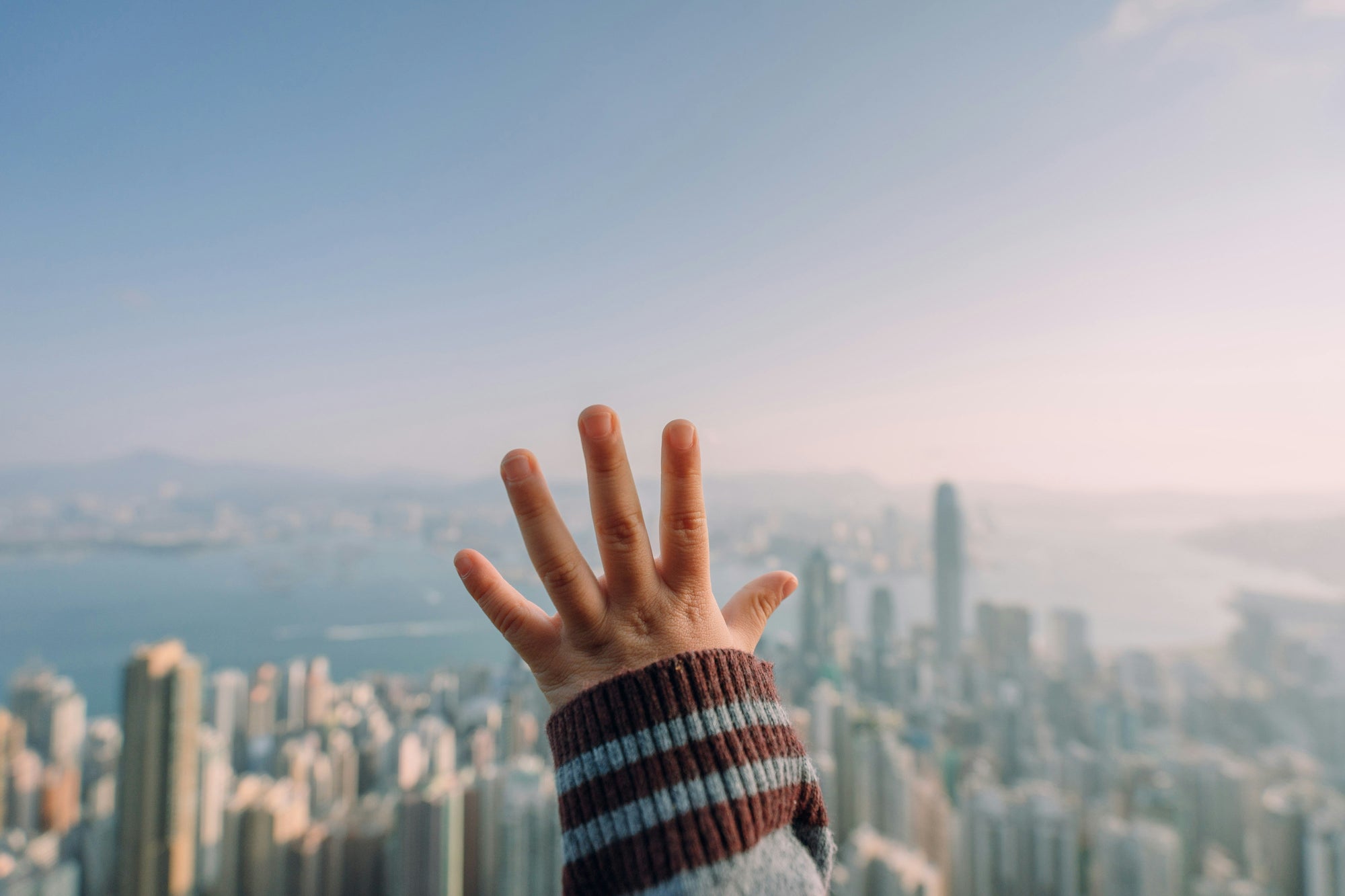 A toddler’s hand pressed against a window, looking out at the skyline of Hong Kong
