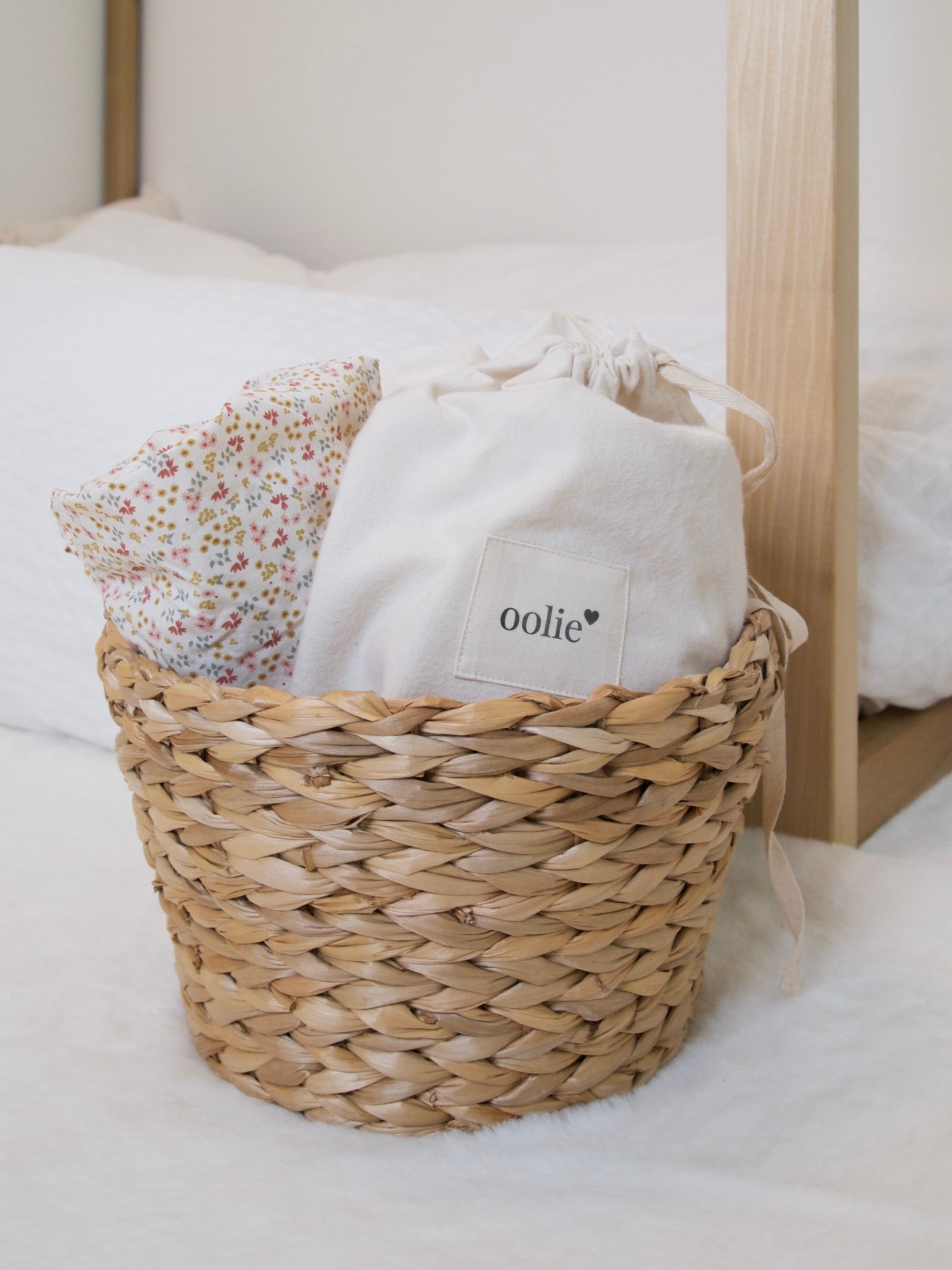 Oolie crib sheets with floral prints rolled into a natural, woven basket, showing a natural organic cotton bag with the Oolie heart logo.