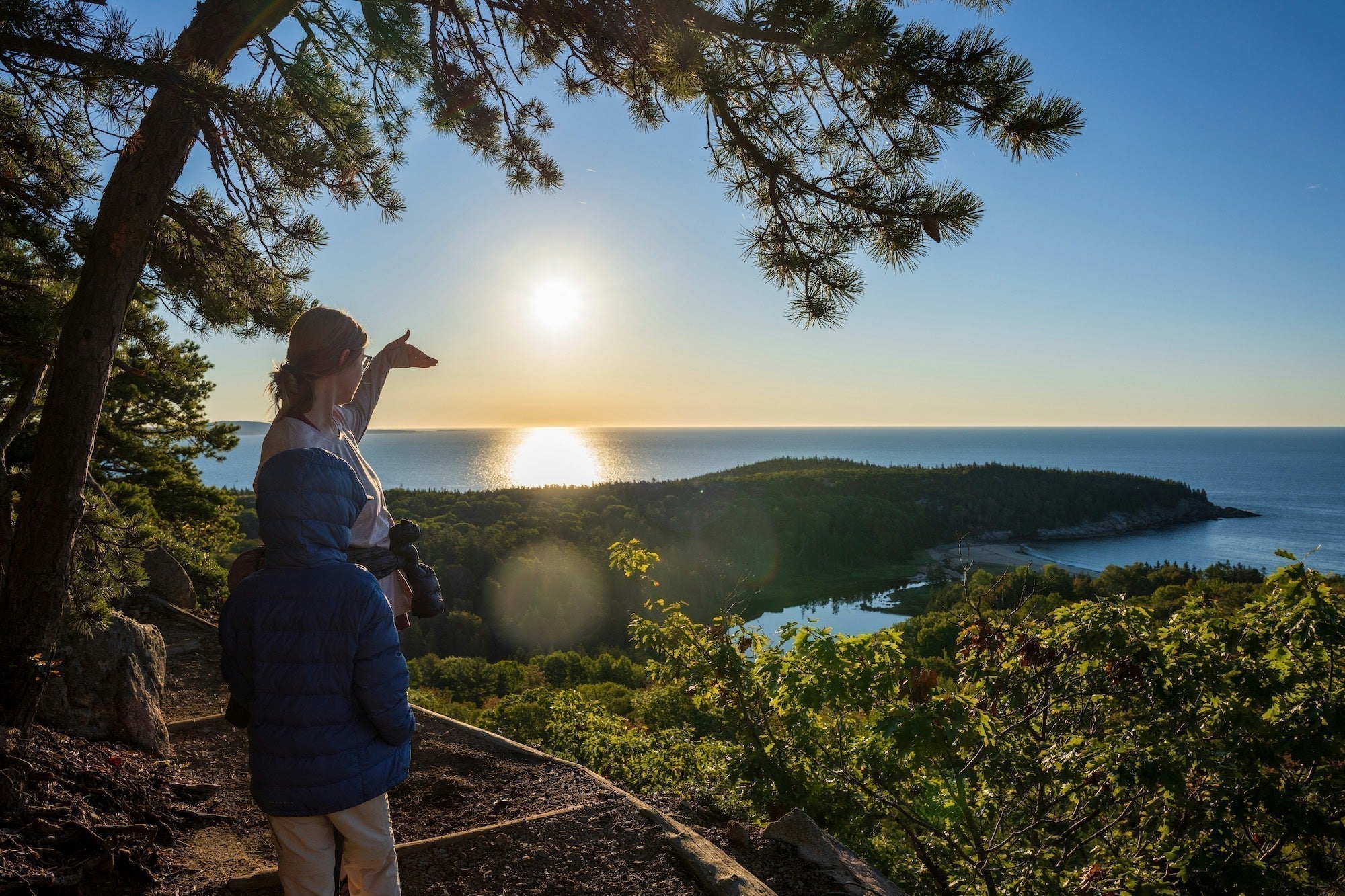 A mom and her son hiking on the Beehive Trail in Acadia National Park, looking out toward the sun rising over the Atlantic Ocean.