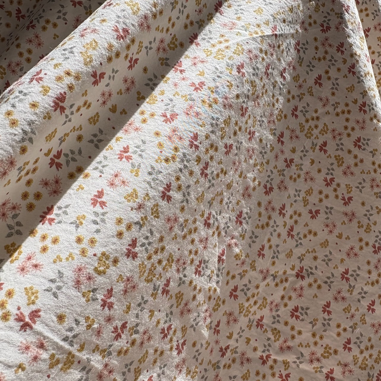 Detail view of Oolie organic cotton crib sheet with prairie ditsy pattern, showing tiny, colorful flowers printed on natural fabric.