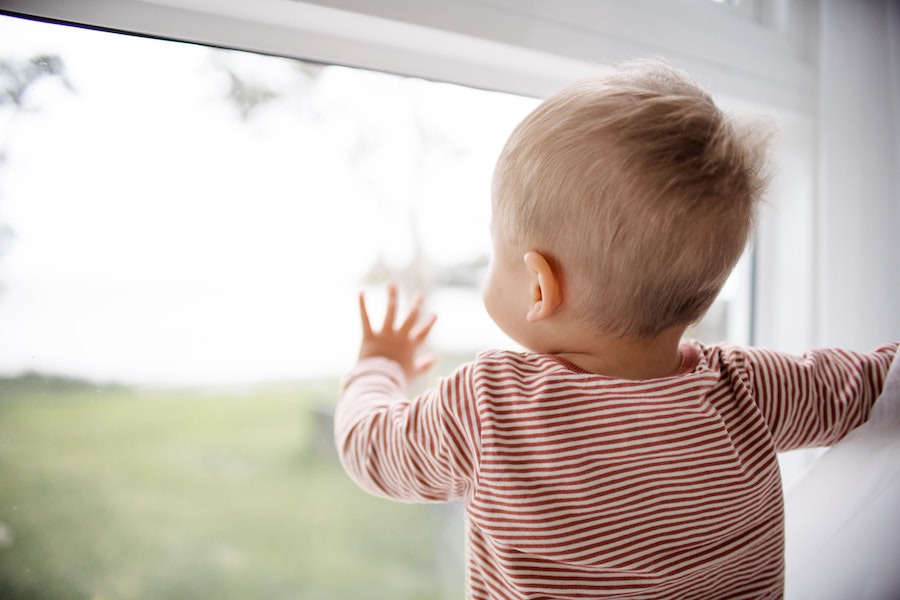 A young child gazing out the window, reaching a hand out toward the sunlight and a green field.