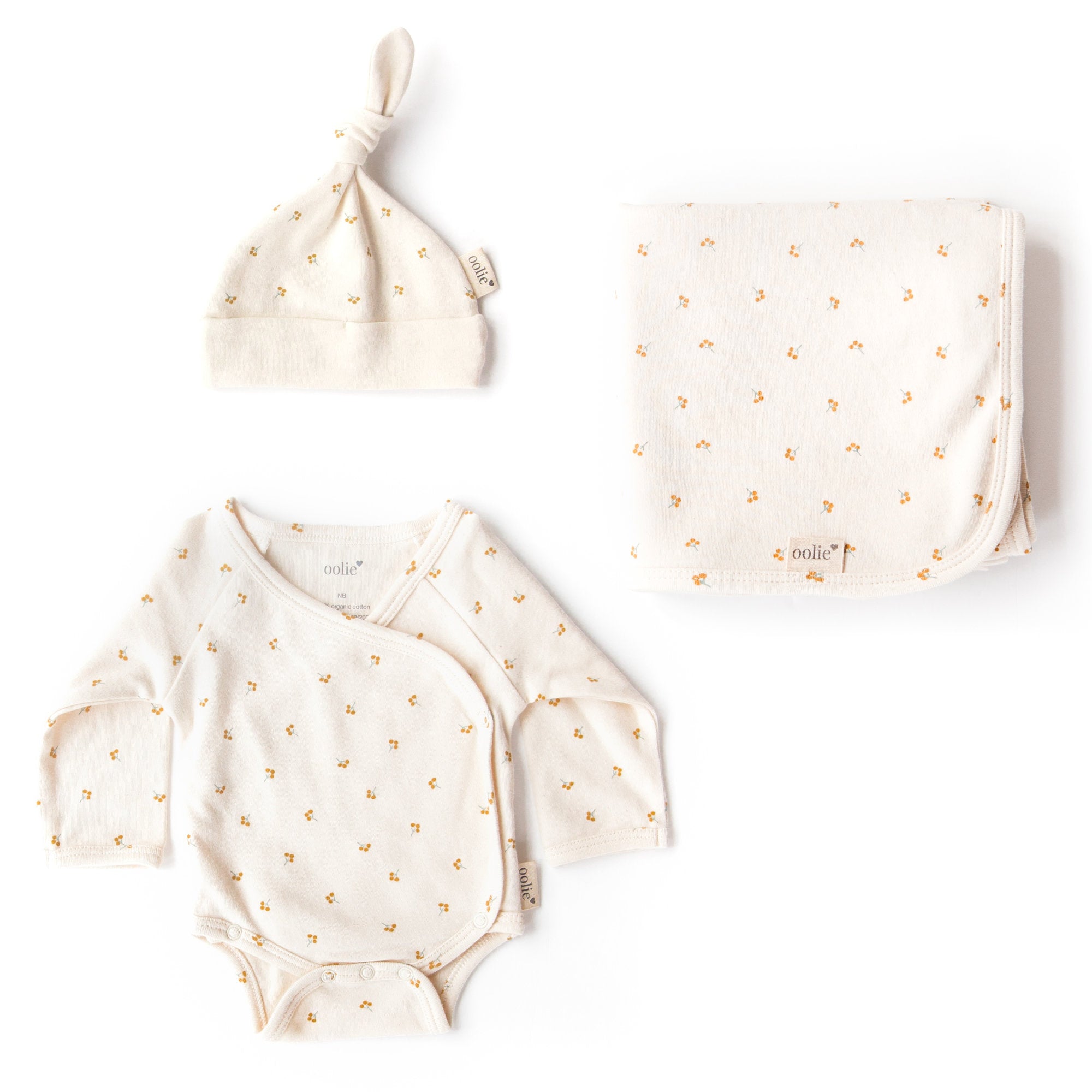 Oolie organic baby hat, baby bodysuit, and baby blanket, laid flat on a white background, each with the gold sprig print, a natural color with small sprigs of golden berries.