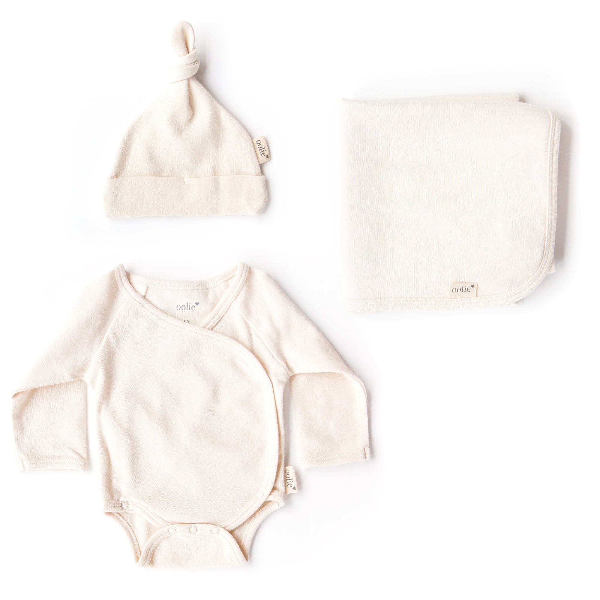 Oolie organic baby hat, baby bodysuit, and baby blanket, laid flat on a white background, each unprinted, revealing the cotton's natural, undyed, unbleached color.