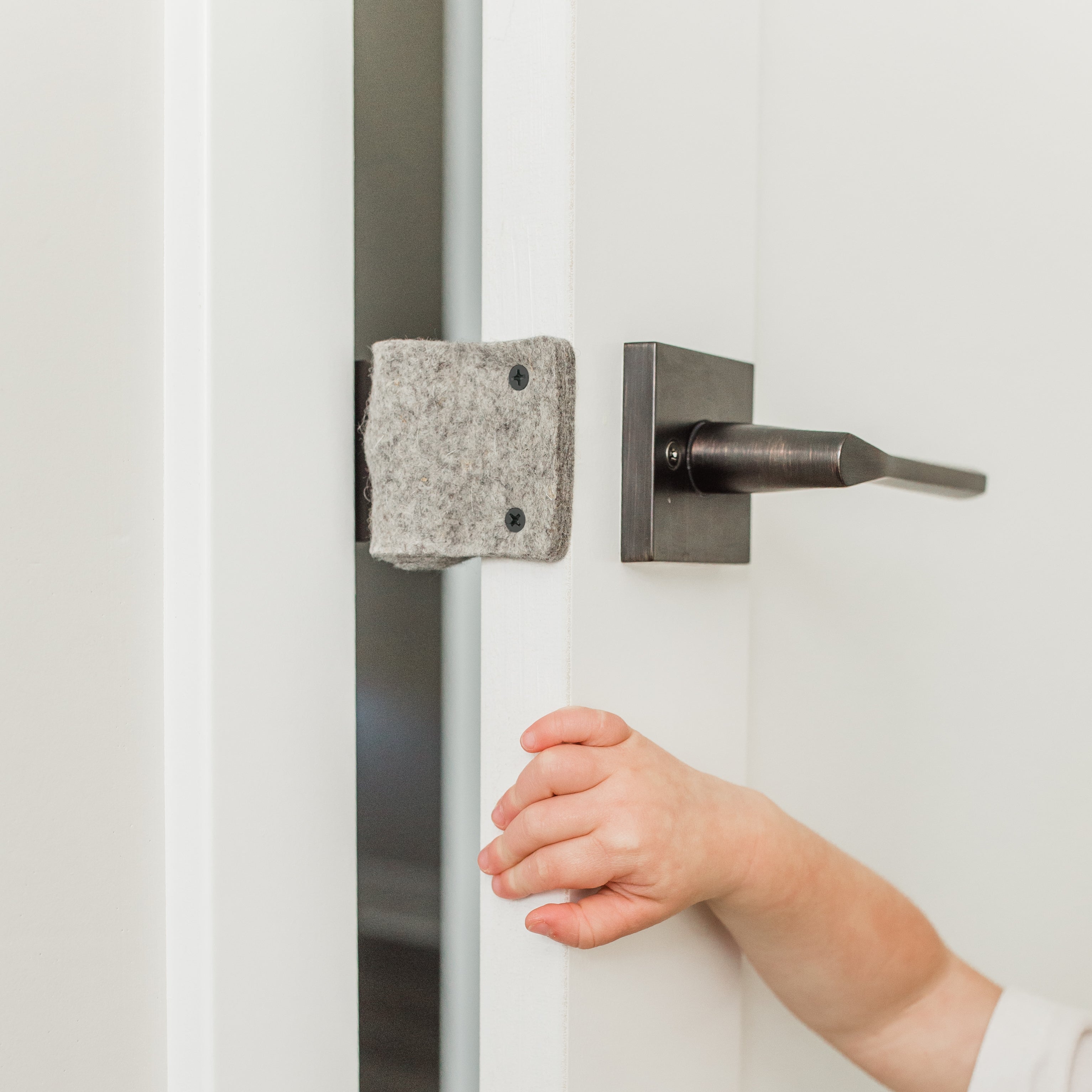 The Oolie Shoosh door silencer and safety bumper shown installed on a door, with a child&#39;s hand holding the door, which is unable to close, due to the bumper.