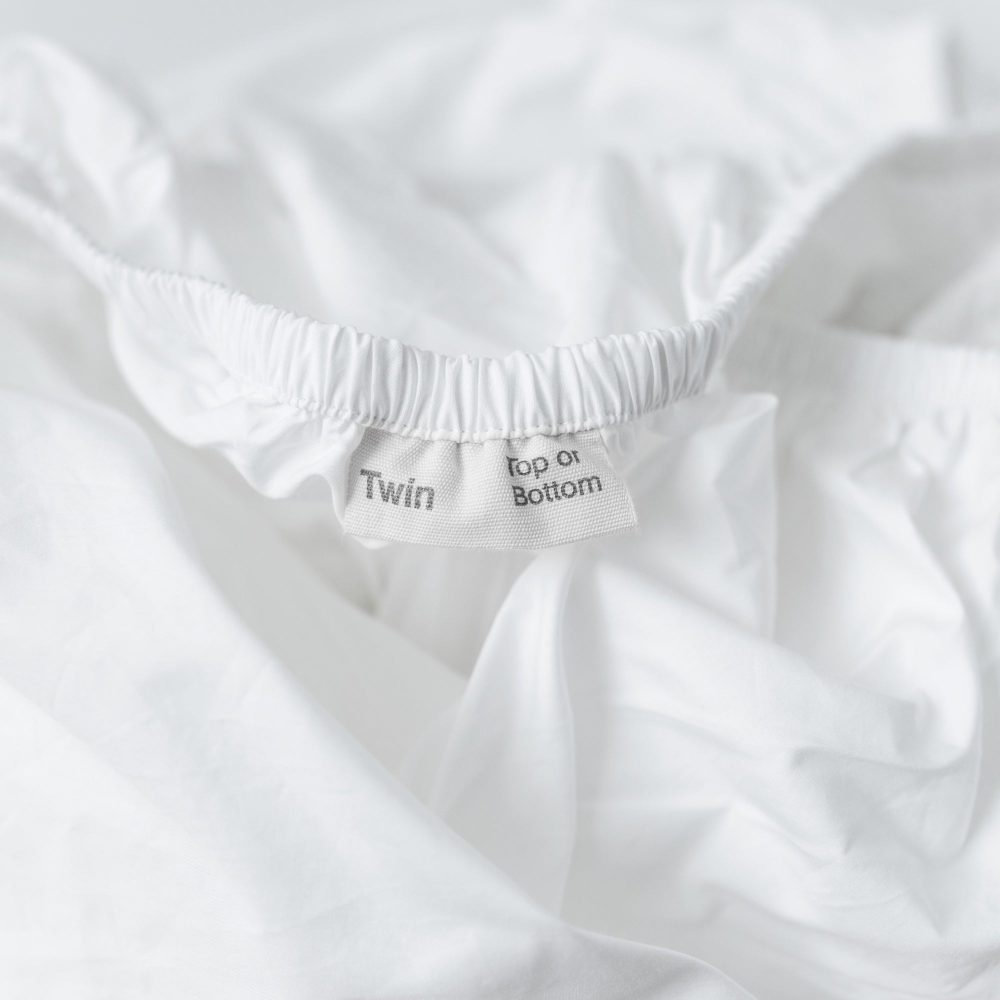A detail view of the orientation label on an Oolie Deep Fitted Sheet, indicating "Twin" size and marking the "Top or Bottom" of the sheet.