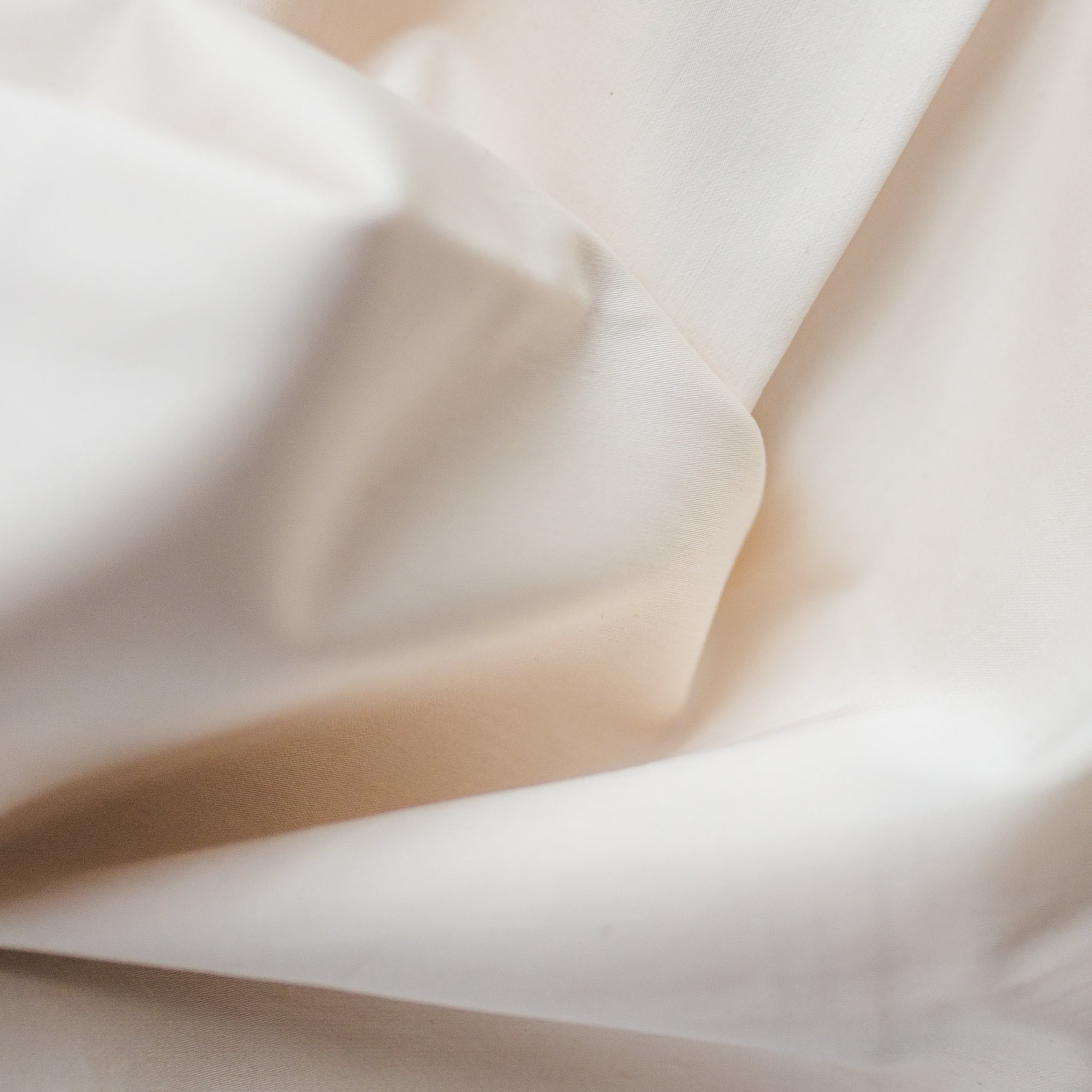 Detail view of the sateen fabric texture and softness, shown in the natural color of undyed and unbleached cotton.