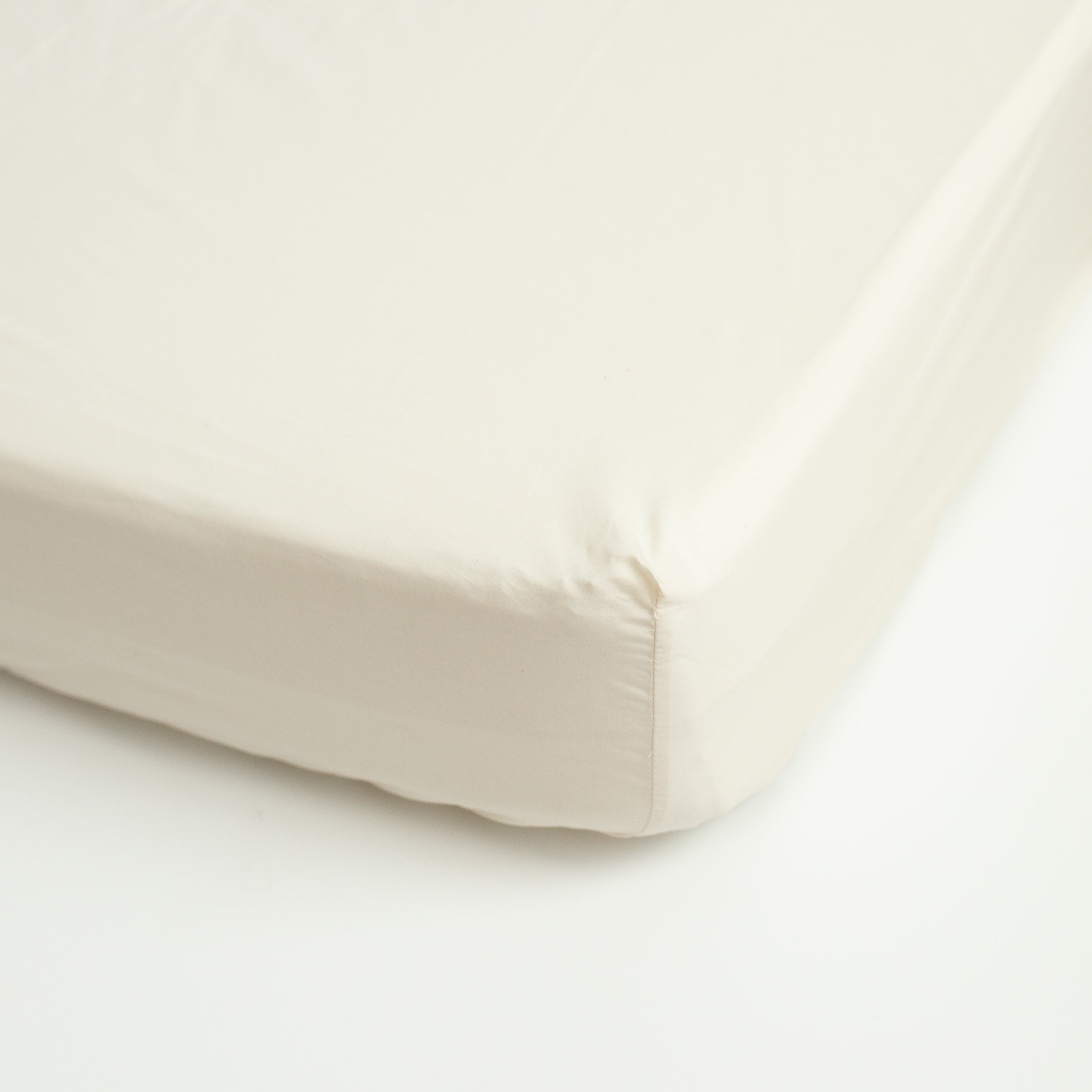 A detail view showing the soft texture of an Oolie deep fitted sheet in natural, unbleached cotton installed on a bed.