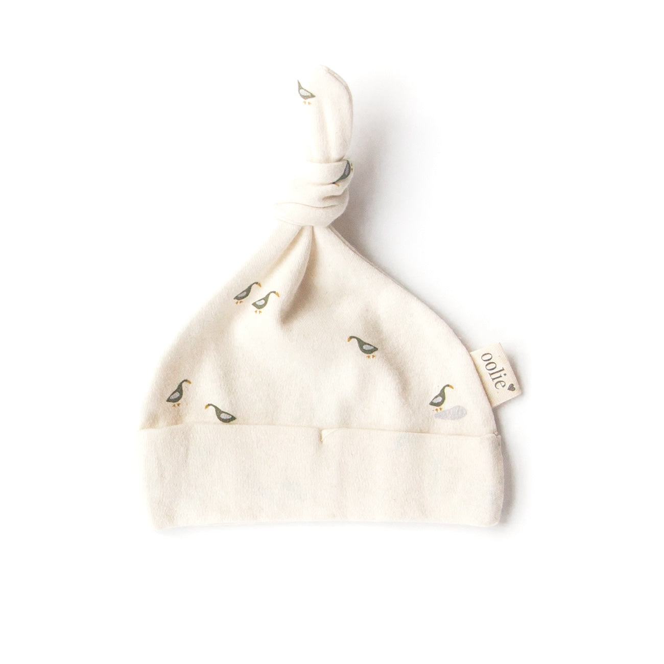 An Oolie organic cotton top knot baby hat with the runner ducks print, a natural color with small green and blue ducks in a repeating pattern.
