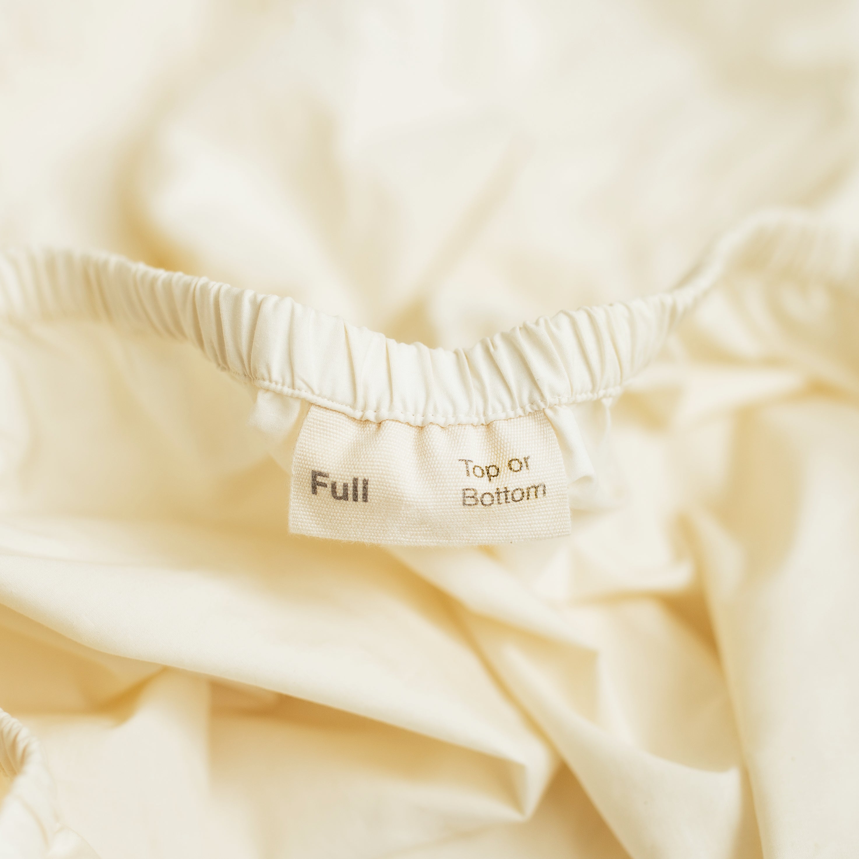 A detail view of the orientation label on an Oolie Deep Fitted Sheet, indicated &quot;Full&quot; size and marking the &quot;Top or Bottom&quot; of the sheet.