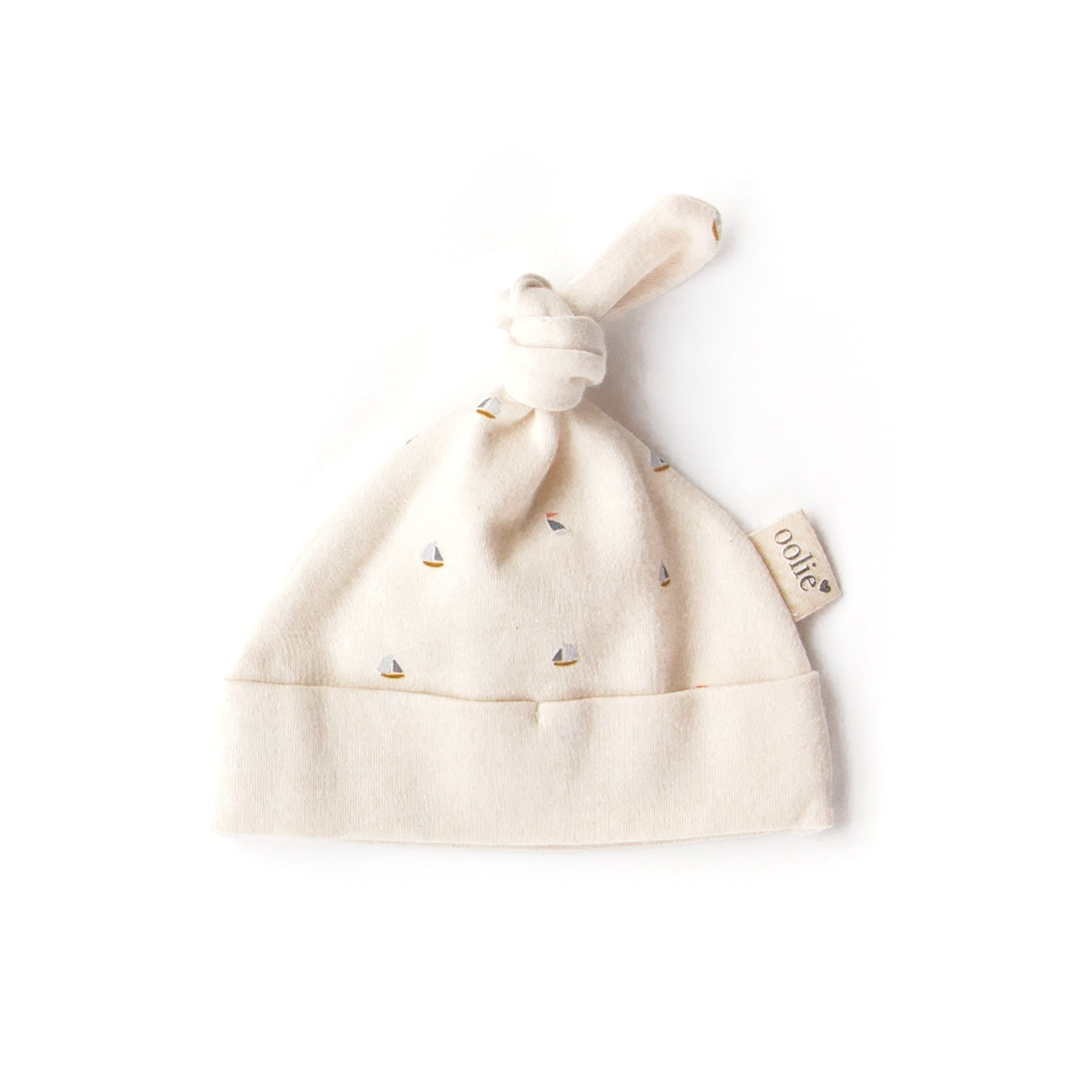 An Oolie organic cotton top knot baby hat with the schooner print, a natural color with small sailboats in a repeating pattern.