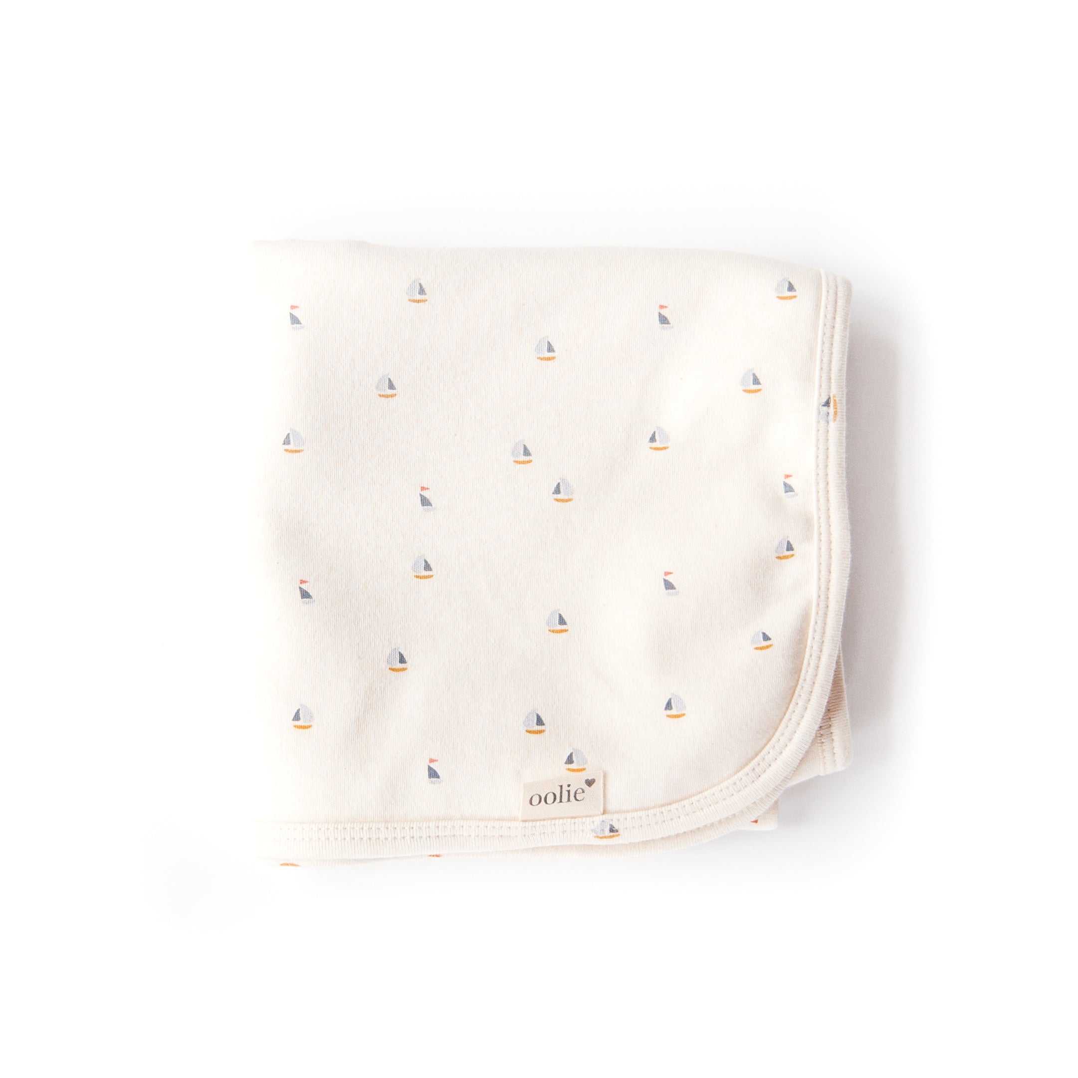 An Oolie organic cotton baby blanket with the schooner print, a natural color with small sailboats in a repeating pattern.