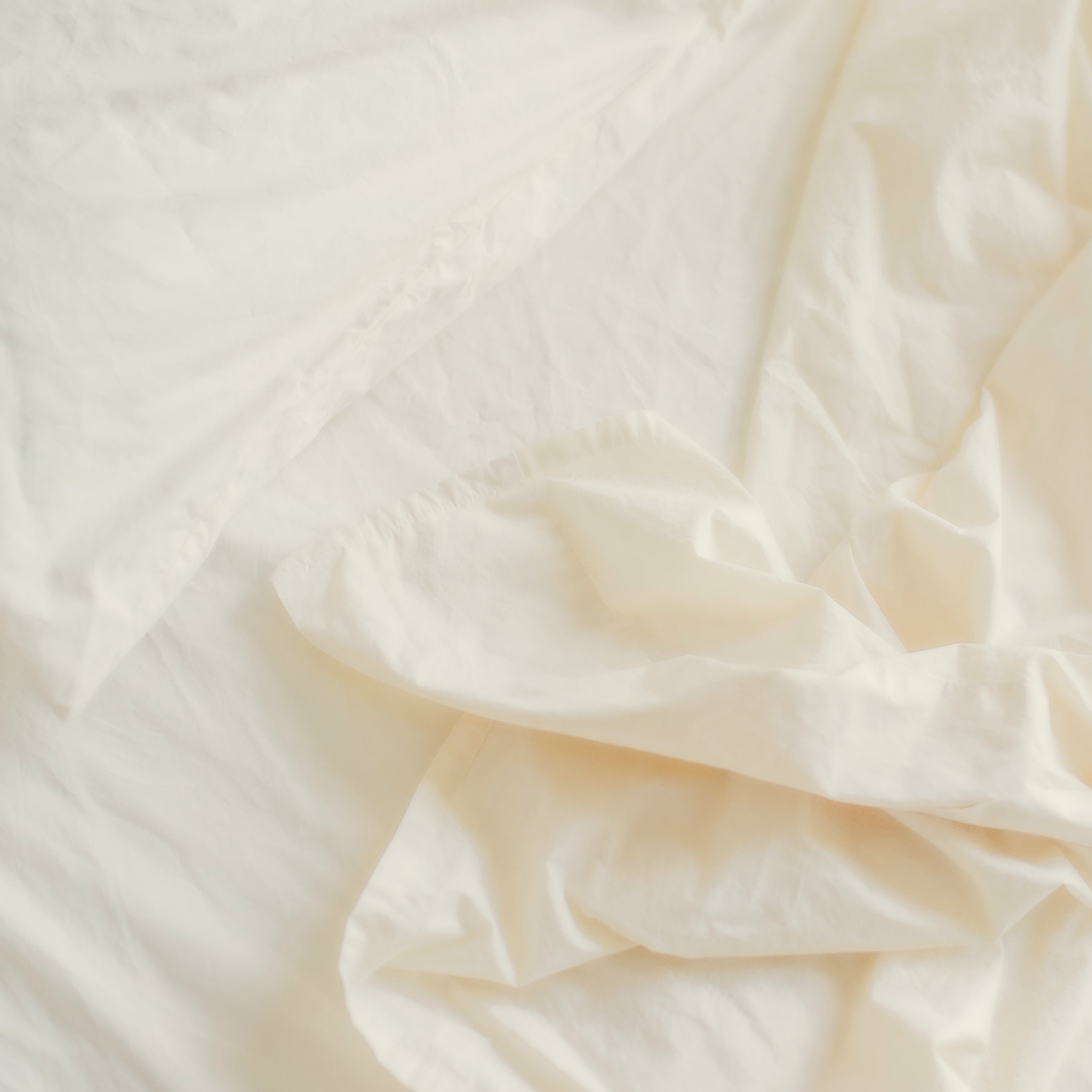 A detail view showing the soft texture of Oolie organic cotton sheets in natural, unbleached cotton installed on a bed.