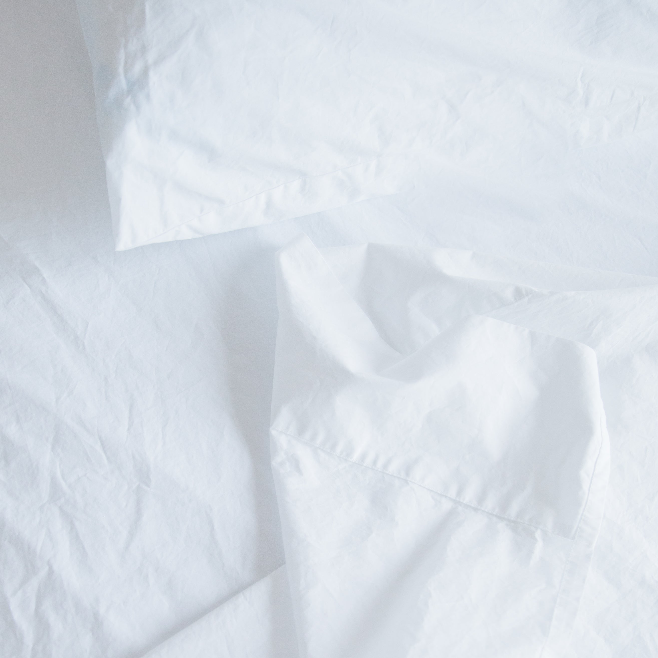 A detail view showing the soft texture of Oolie organic cotton sheets in white cotton installed on a bed.