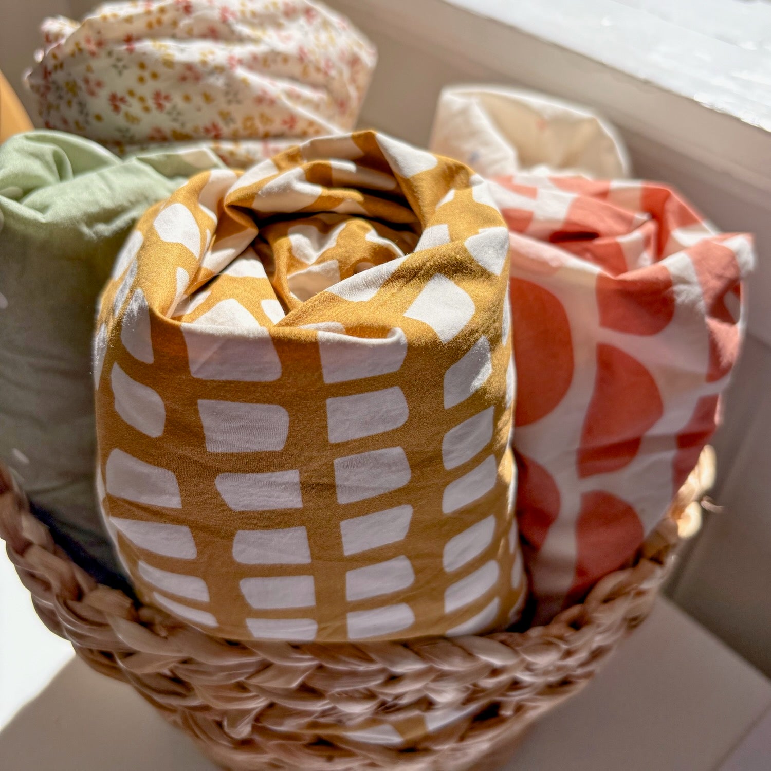 Organic cotton crib sheets with graphic prints rolled up in a basket
