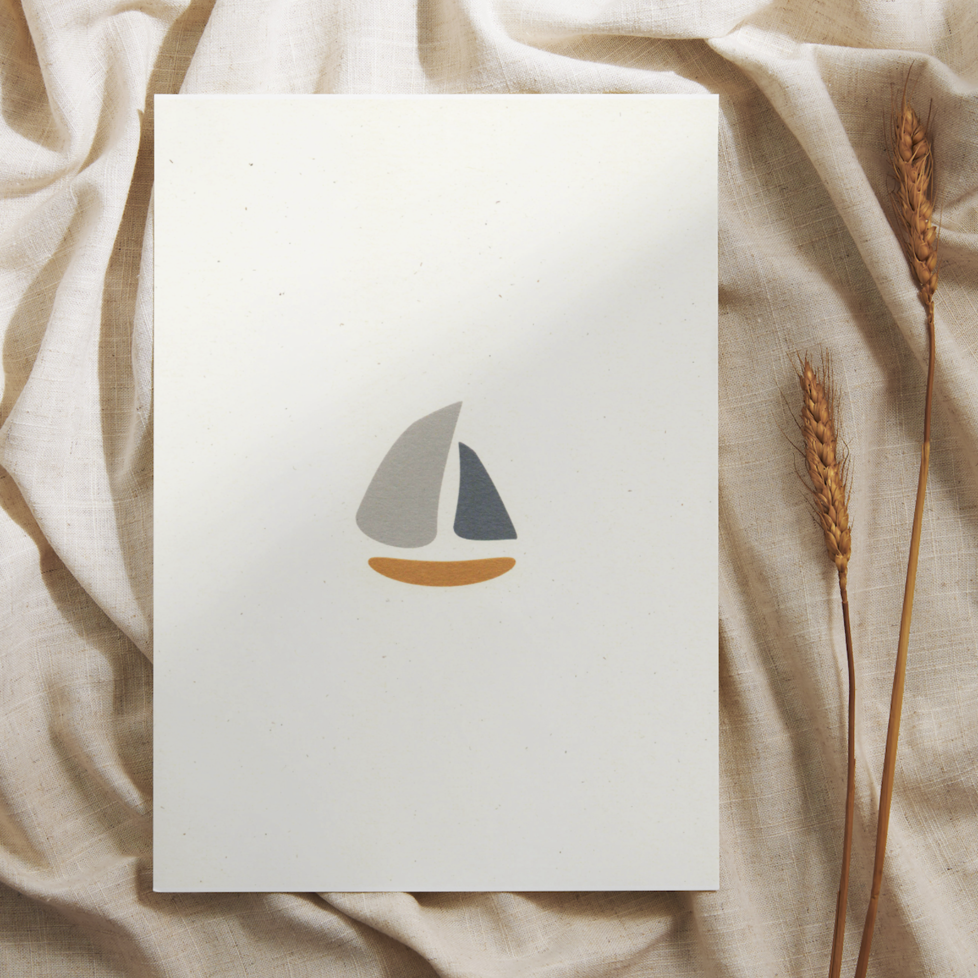 A cute nursery print of a schooner or small sailboat on recycled, natural paper, set on a backdrop of natural linen and wheat.