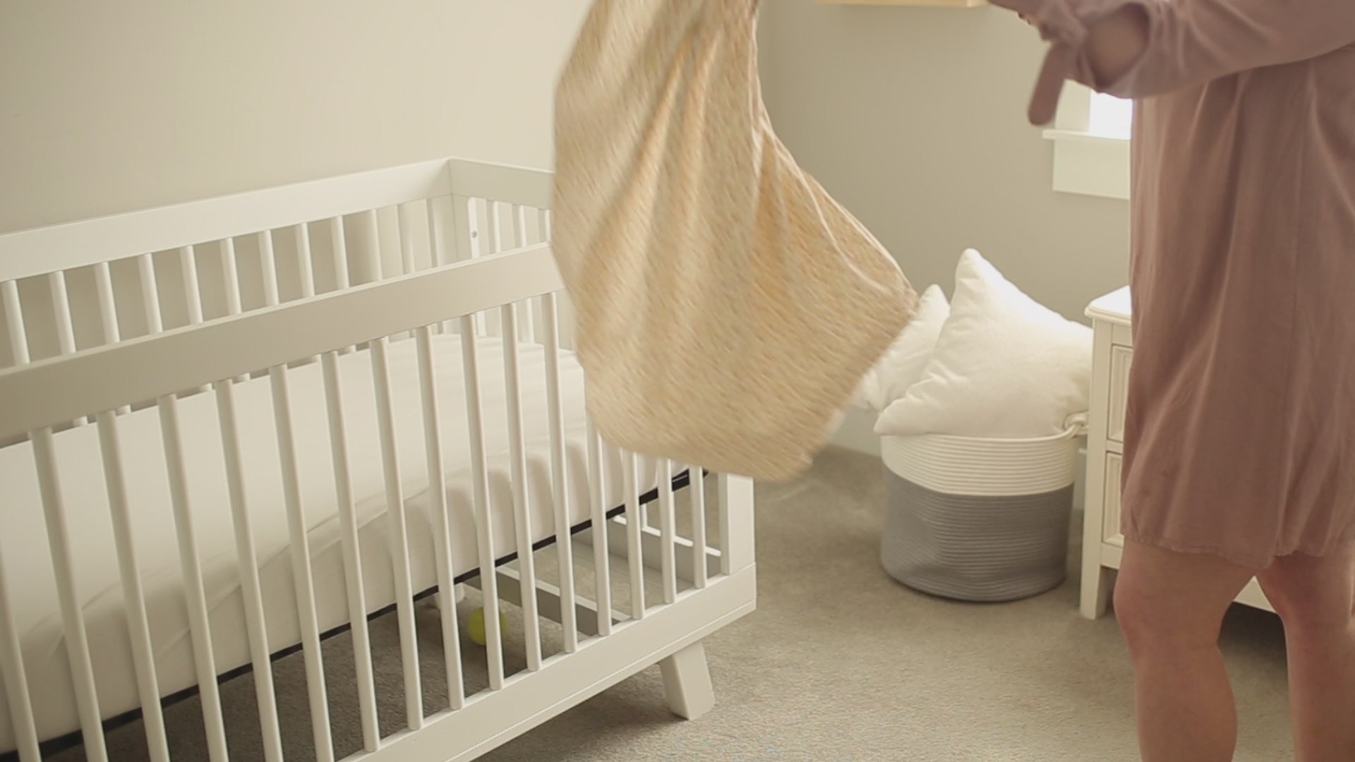 Video of a mother installing an Oolie organic cotton crib sheet onto a mattress, then snuggling her new baby and laying him down gently in the crib.